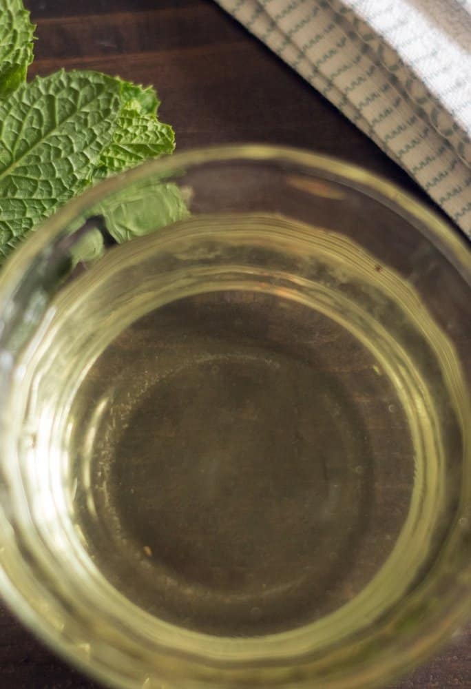 an aerial view of homemade simple syrup in a clear bowl with a sprig of mint to the left of the bowl
