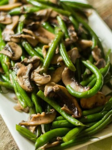 Green beans mushrooms with shallots on a white rectangular plate.