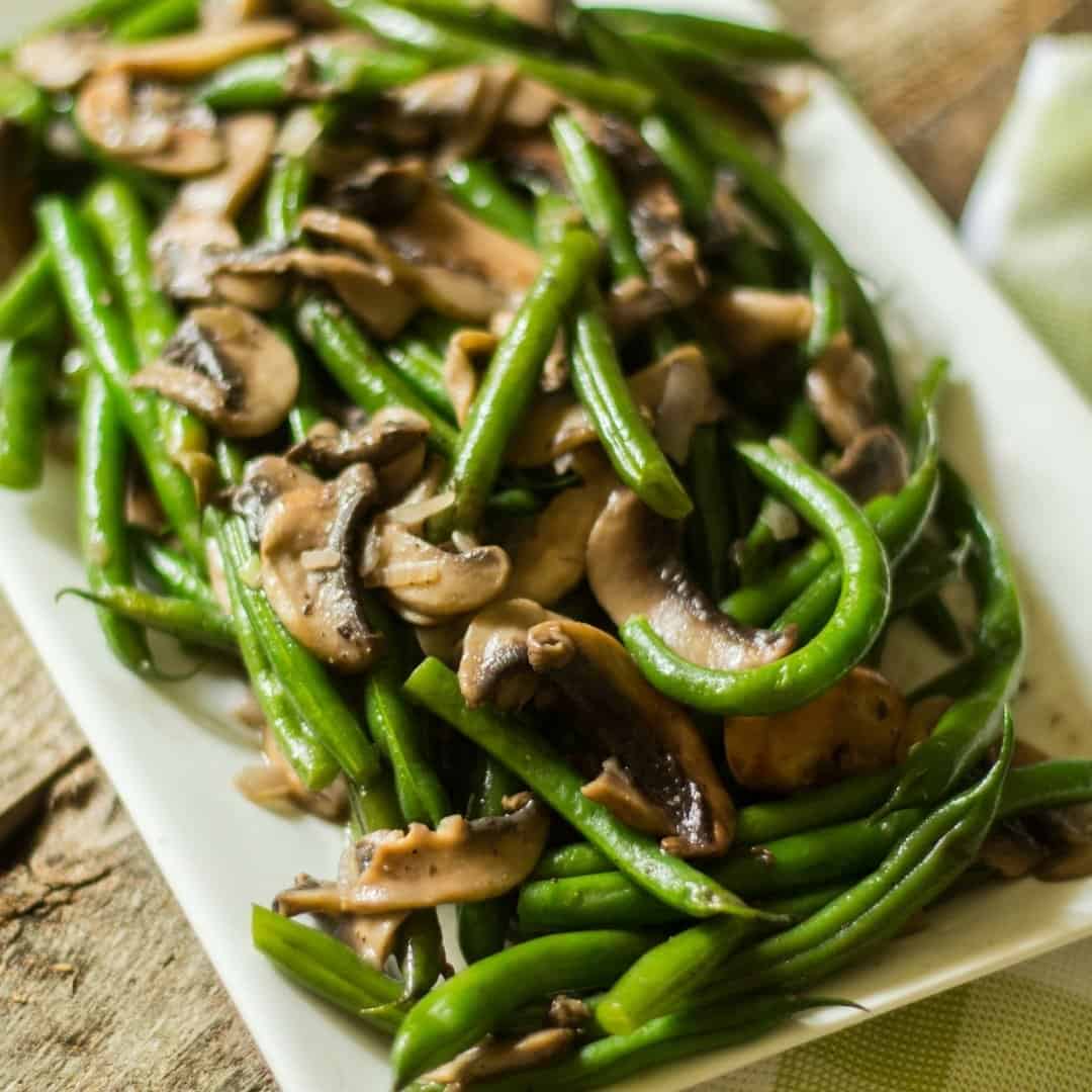 Green beans mushrooms with shallots on a white rectangular plate.