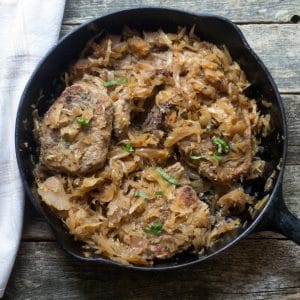 overhead photo of baked pork chops smothered with sauerkraut in a cast iron pan.