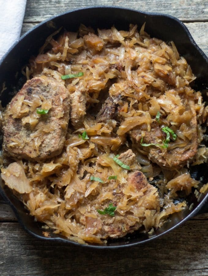 overhead photo of baked pork chops smothered with sauerkraut in a cast iron pan.