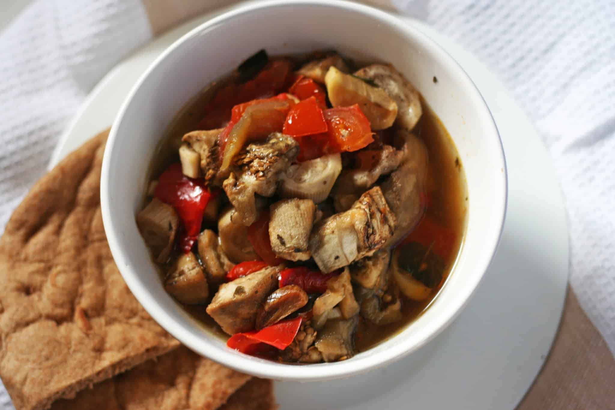 Tender eggplant and peppers slow cooked and served in a white bowl with warm pita bread in a side plate