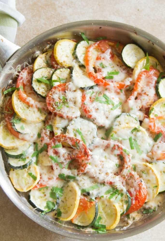 An overhead shot of zucchini tomato bake in a large siver saute pan that has been roasted in the oven with melted mozzarella cheese on top of the veggies