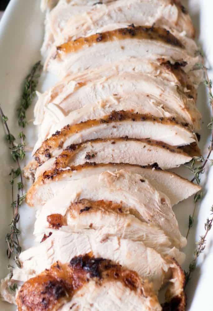Roasted Turkey breast that has been sliced with fresh thyme on a white platter.