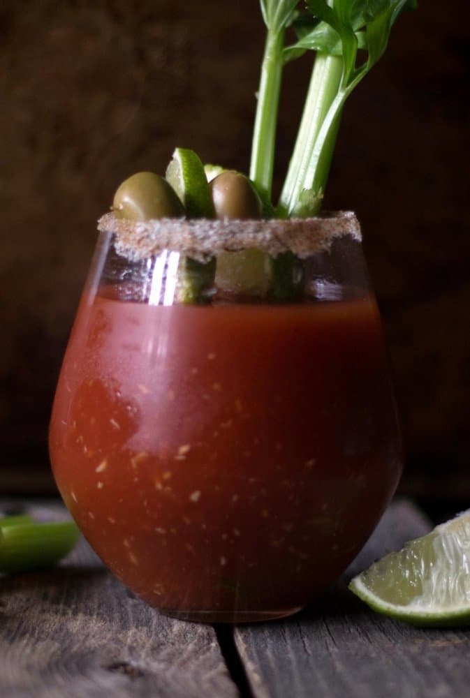 The perfect bloody mary topped with lime wedge, olives, celery in a glass rimmed with salt.