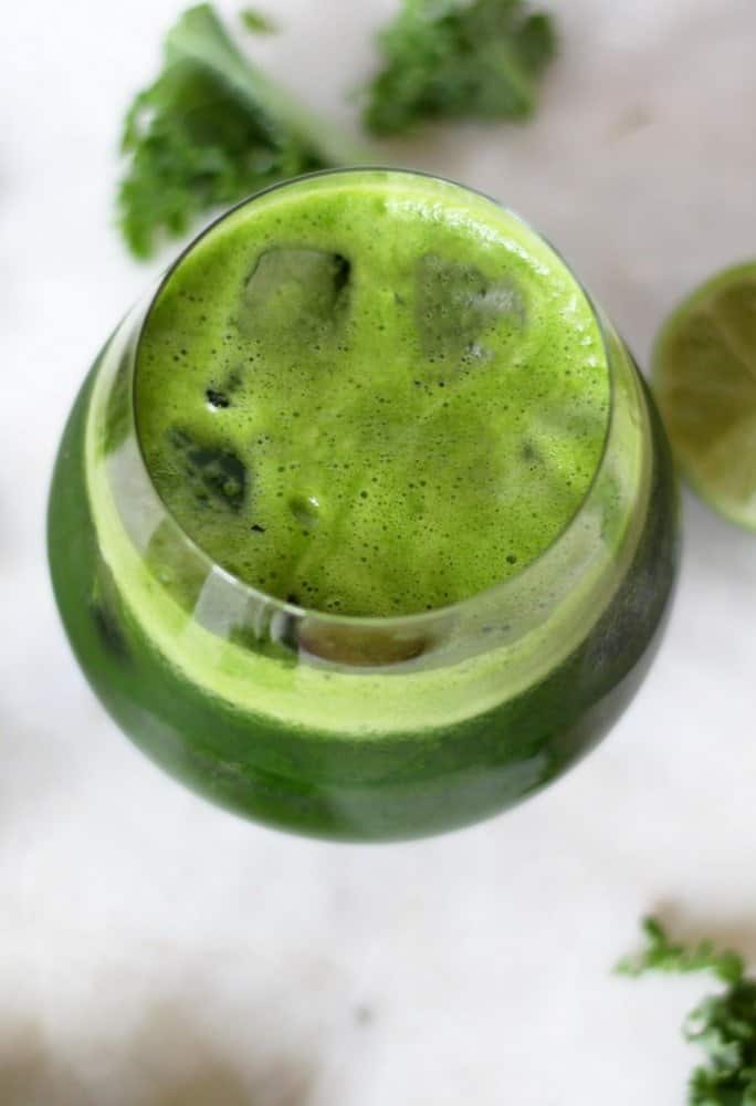  green detox juice in a clear glass with kale leaves sprinkles on the tqble.