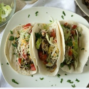 an overhead shot of crockpot beef tacos loaded with lettuce, cheese and tomatoes