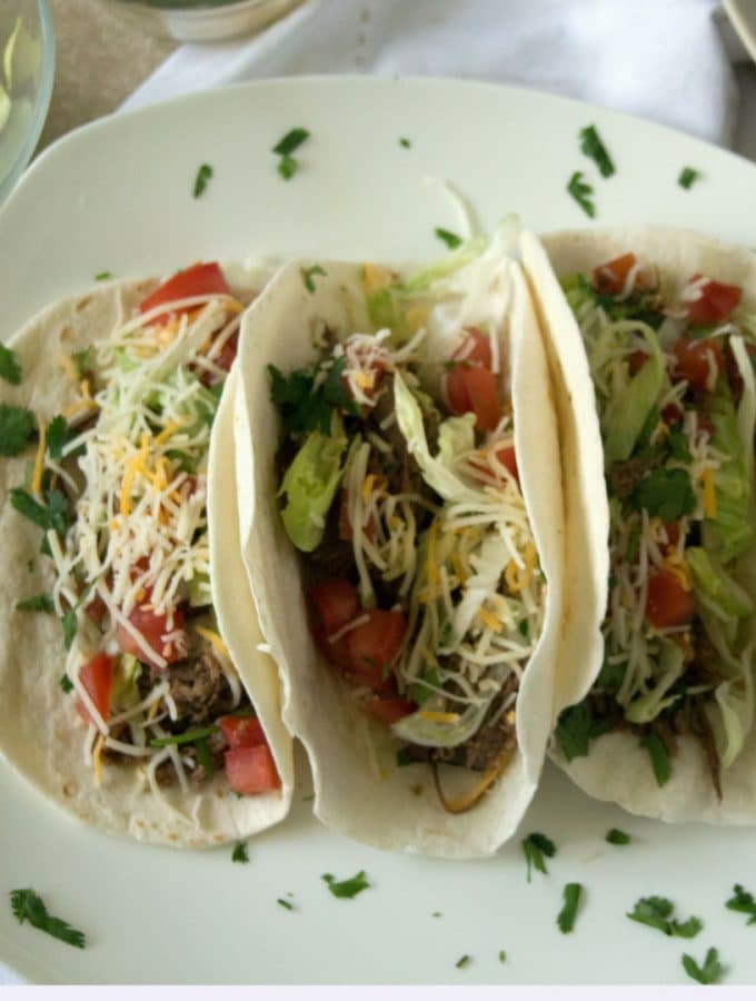 an overhead shot of crockpot beef tacos loaded with lettuce, cheese and tomatoes