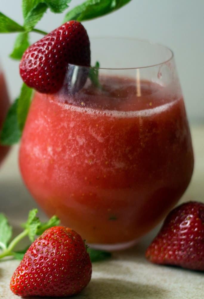 A side view of a vodka strawberry drink vodka slush cocktail that has been blended and garnished with a slice of strawberry and mint