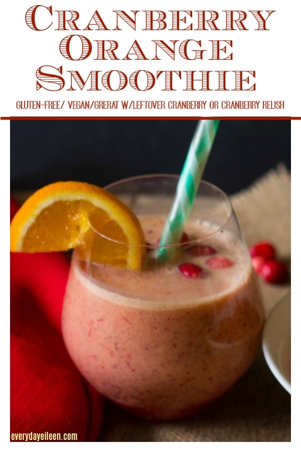 Cranberry orange smoothie in a clear glass garnished with orange and fresh cranberries around the glass.