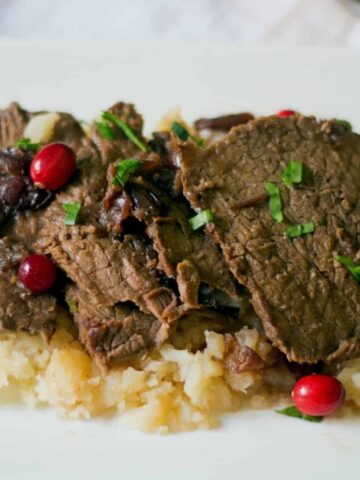 slow cooker cranberry pot roast on top of the best mashed potatoes They are drizzled with the pot roast gravy and chopped parsley