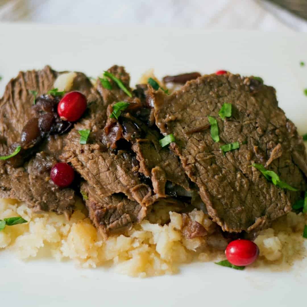 slow cooker cranberry pot roast on top of the best mashed potatoes They are drizzled with the pot roast gravy and chopped parsley
