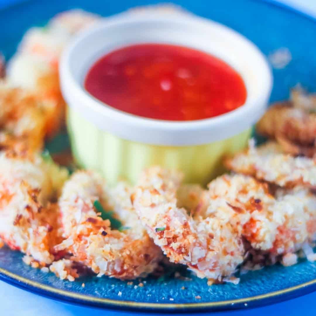 Healthy Coconut Shrimp with Orange Dipping Sauce in a yellow bowl in the middle of a blue speckled platter.