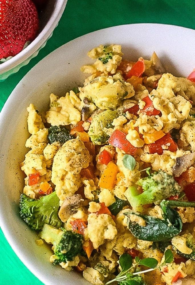 An aerial view of broccoli, spinach, tomatoes and zucchini scrambled with eggs and seasoned with black pepper in a white bowl with a green background
