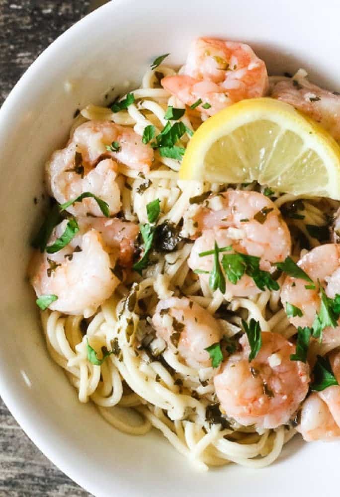 An aerial view of shrimp scampi with lemon and pasta with parsley sprinkled on top of the meal