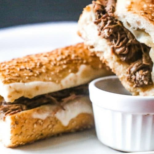 warm slow cooker french dip sandwich with melted provolone cheese dipped into a au jus sauce
