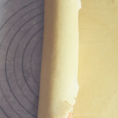 An aerial view of an all butter pie crust that has been rolled out and is rolled onto a rolling pin. The flaky pie dough with then be rolled out into a pie pan.