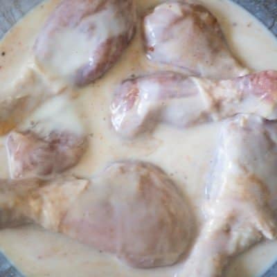 An aerial view of buttermilk baked chicken drumsticks in a clear bowl, marinating in spicy seasoned buttermilk.