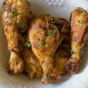 An aerial view of baked crispy chicken drumsticks in an ivory bowl.