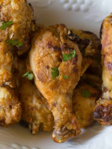 An aerial view of baked crispy chicken drumsticks in an ivory bowl.