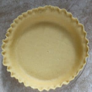 An aerial view of a buttery pie crust recipe in a clear pie pan with fluted edges that is not yet baked