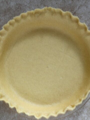 An aerial view of a buttery pie crust recipe in a clear pie pan with fluted edges that is not yet baked