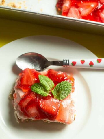 overhead view of strawberry pretzel dessert recipe with mint leaves on top on a white dessert plate with a spoon on top of plate with strawberries on the handle