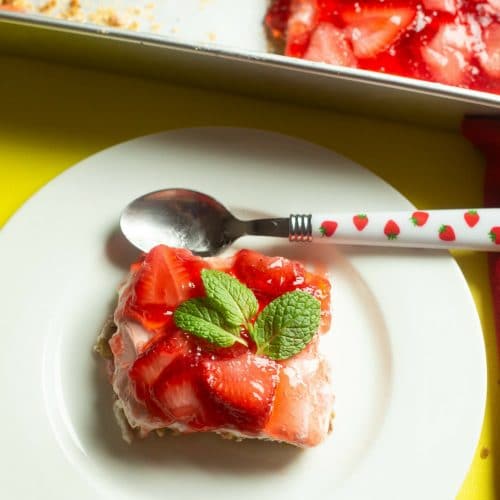 overhead view of strawberry pretzel dessert recipe with mint leaves on top on a white dessert plate with a spoon on top of plate with strawberries on the handle