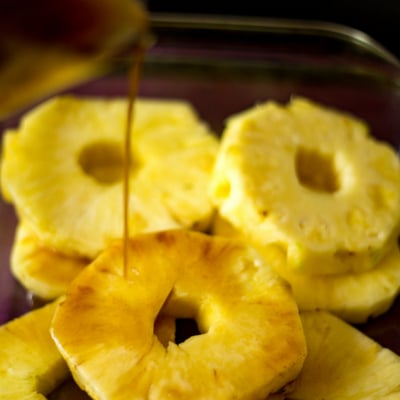 a juicy platter or pineapple slices with rum sauce being drizzled over the slices to marinate before grilling.