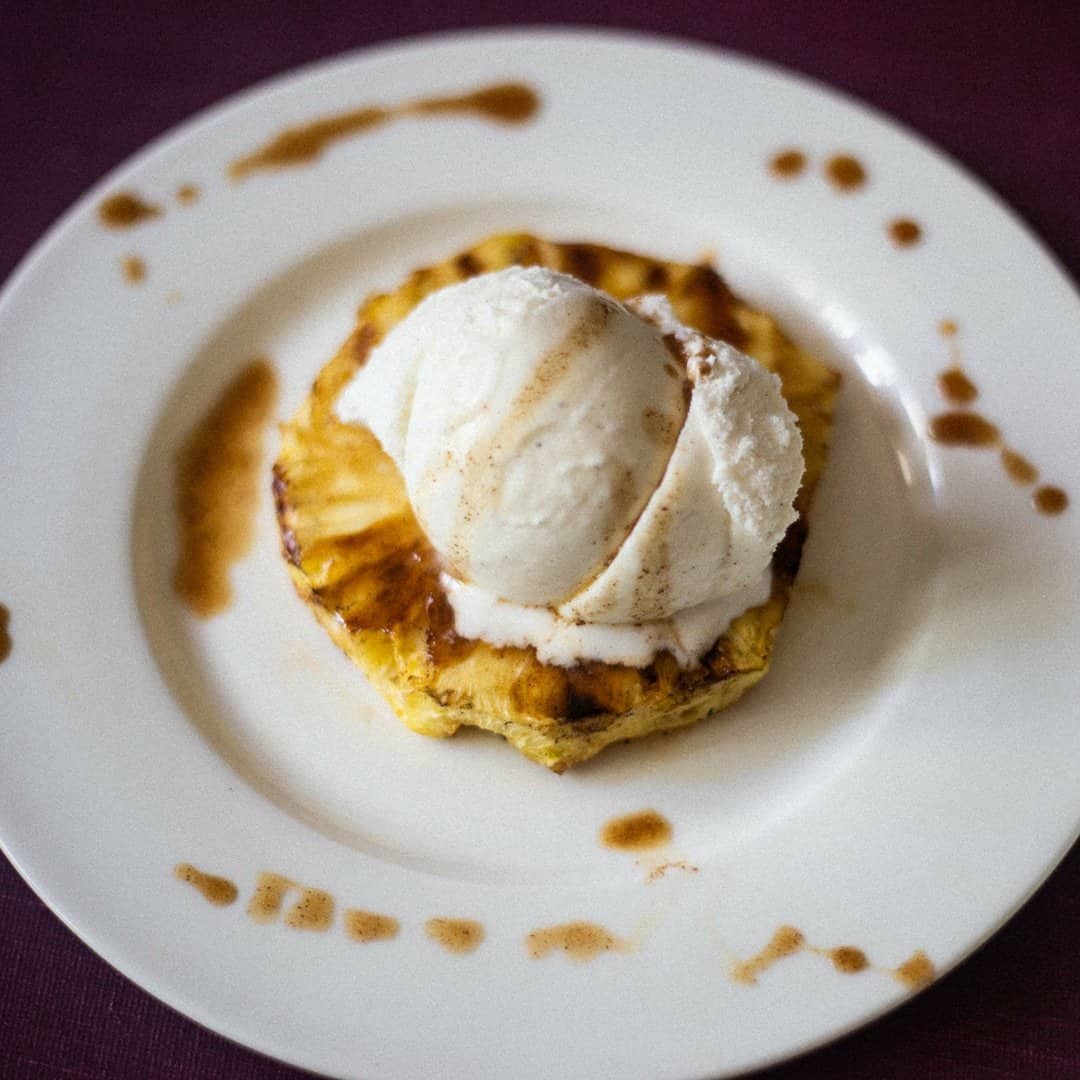 Grilled pineapple topped with a big scoop of fresh vanilla ice cream with rum sauce sprinkled around the white plate.