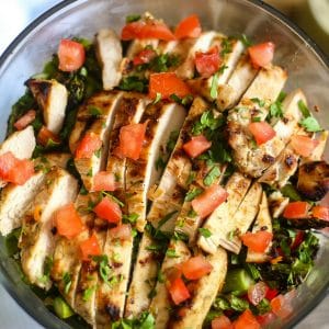 Layered grilled chicken asparagus salad in a large glass bowl topped with vine ripe tomatoes and chopped parsley.