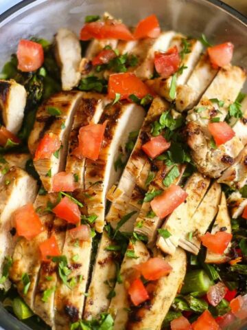 Layered grilled chicken asparagus salad in a large glass bowl topped with vine ripe tomatoes and chopped parsley.