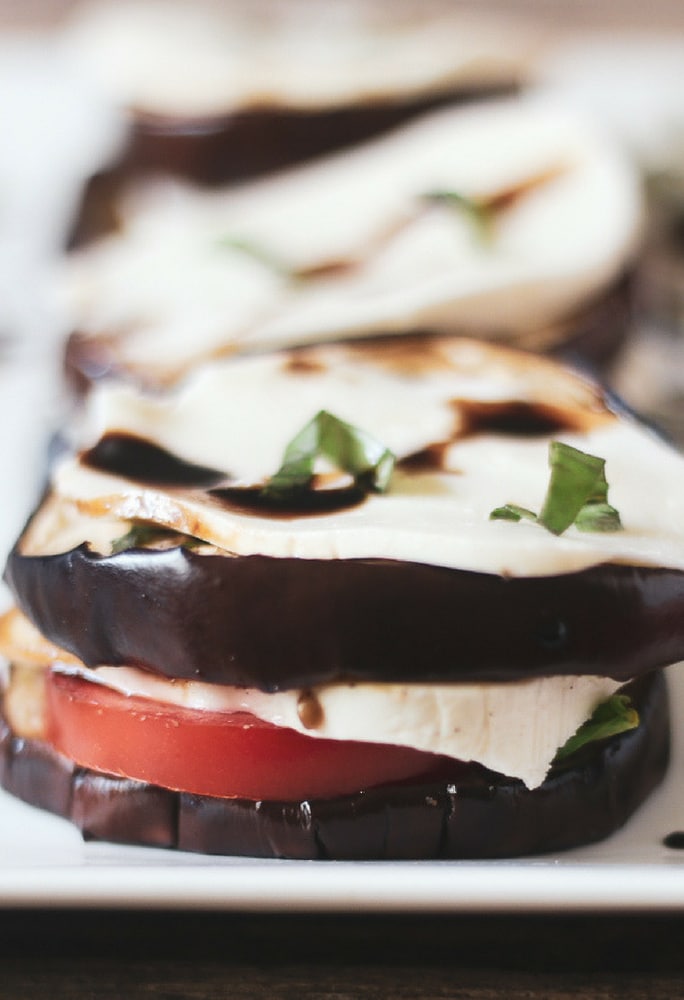 A delicious grilled eggplant Caprese salad stacked with juicy tomatoes, balsamic glaze, fresh sliced mozzarella with a chiffonade of basil topping the eggplant stack