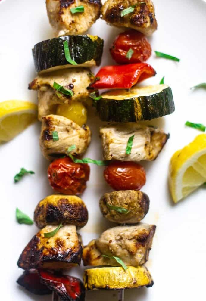 overhead view of grilled citrus marinated chicken kabobs on a metal skewer with zucchini, tomatoes, and mushrooms