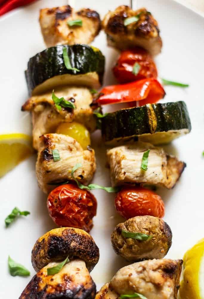 Grilled Chicken Shish Kabobs and vegetables with a citrus marinade on skewers that have been grilled on a white platter with with chopped parsley and lemon wedges
