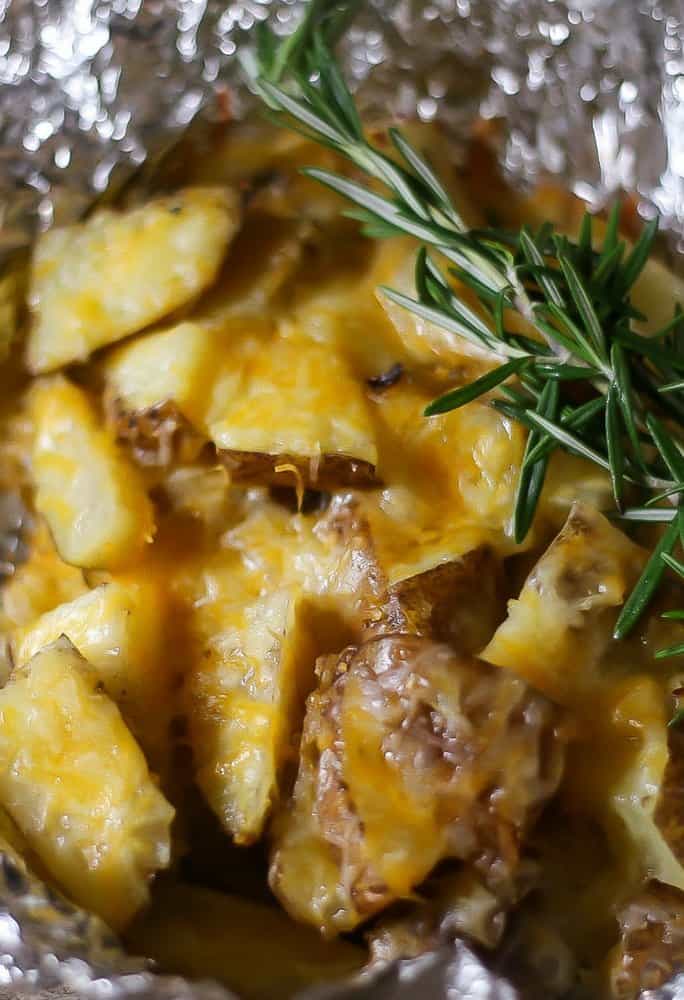 Cheesy grilled foil packet potatoes on aluminum foil that have been grilled with fresh rosemary and ready to eat!