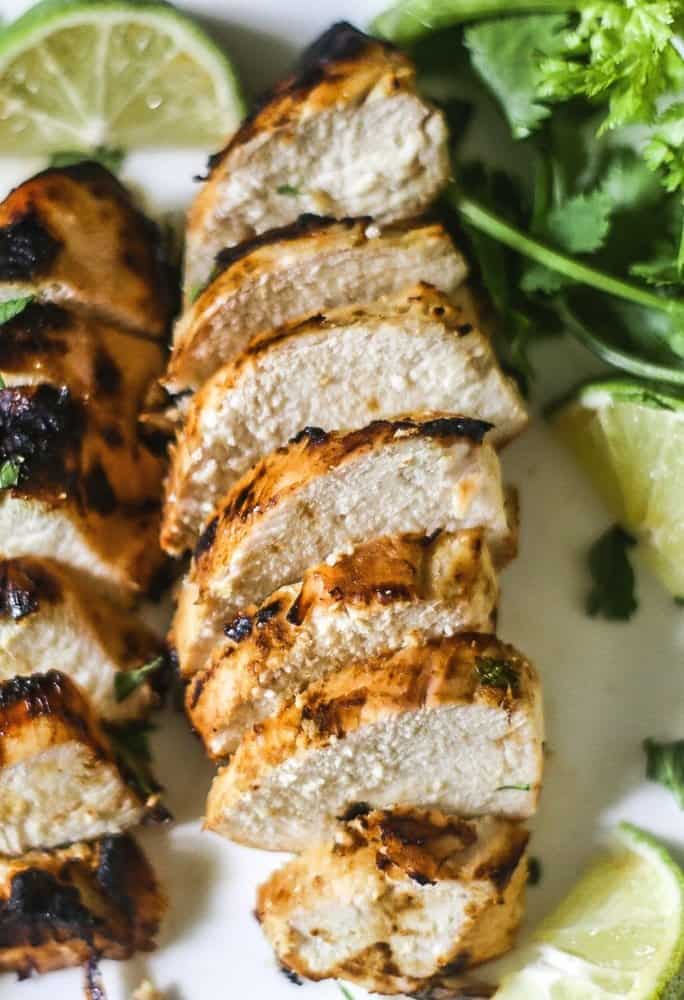 Grilled Dijon Lime Chicken on a white platter with cilantro and limes around the sliced chicken.