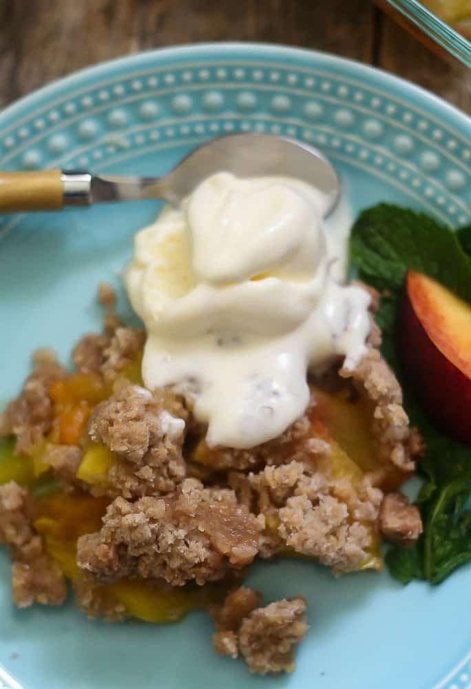 The best warm peach crumble topped with vanilla ice cream that is melting into the amazing flavors of the fruit cobbler.