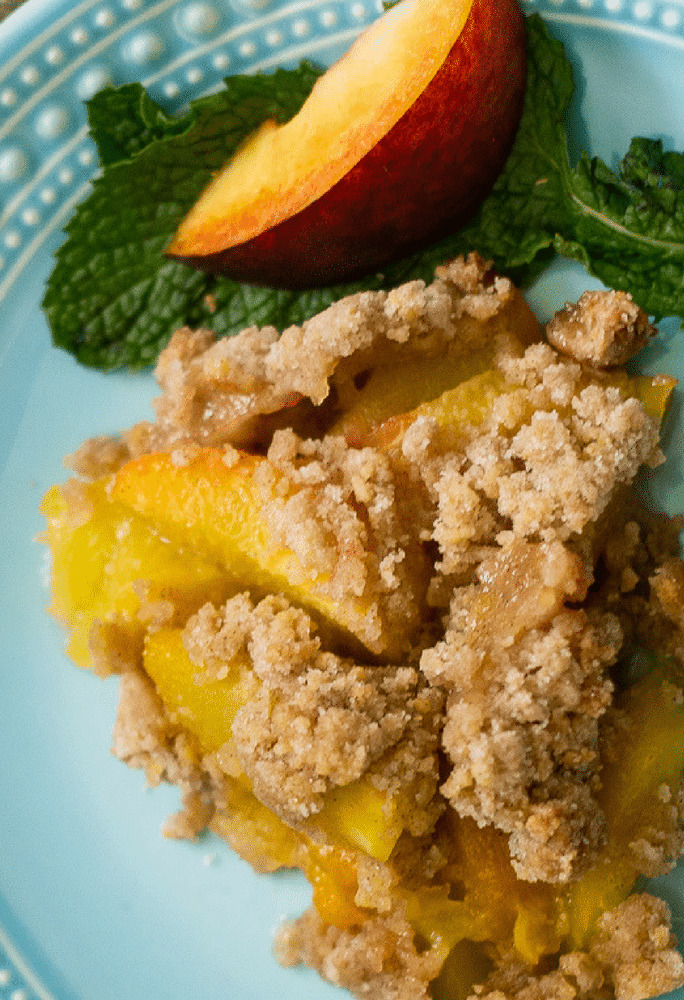Delicious peach cobbler served on a sky blue platter with fresh peaches on the side of the dessert plate