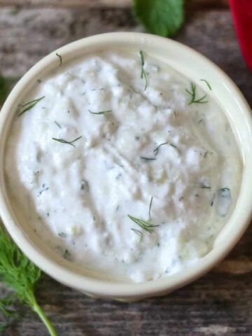 homemade tzatziki sauce with fresh dill sprinkled on top in a white bowl with a sprig of dill to the side of the dip bowl.