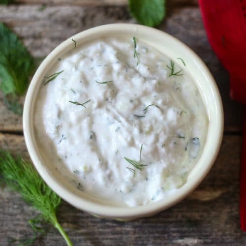 homemade tzatziki sauce with fresh dill sprinkled on top in a white bowl with a sprig of dill to the side of the dip bowl.