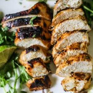 Overhead view of tasty grilled marinated chicken breasts, made with Dijon mustard, lime juice, garlic, herbs and spices on a white plate with lime wedges and herbs sprinkled on the platter