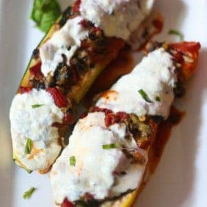 baked vegetable lasagna stuffed zucchini on a white plate with meted fresh mozzarella cheese on top and a sprinkling of parsley all around the plate.