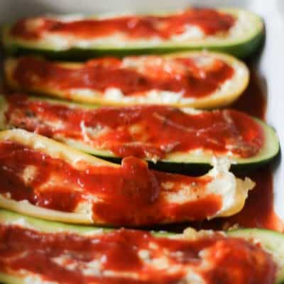 Zucchini is prepped for toppings. The zucchini halves each have ricotta cheese mixture, then marinara. the veggie toppings are on their way.