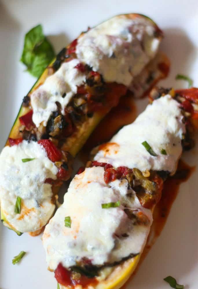 Vegetable lasagna stuffed zucchini boats on a white plate that has been roasted and topped with fresh mozzarella that has melted in the veggies and zucchini boat.