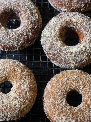 Four baked apple cider donuts with a cinnamon sugar topping on a black mesh rack.