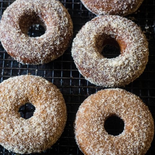 Four baked apple cider donuts with a cinnamon sugar topping on a black mesh rack.