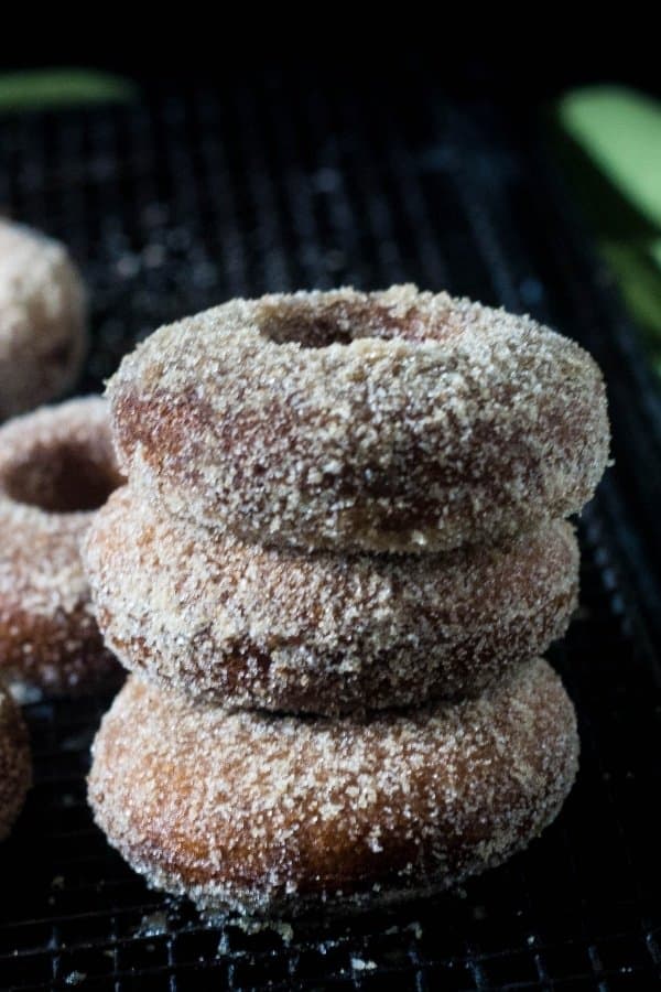 Baked apple cider donuts with cinnamon sugar stacked on a cooling rack