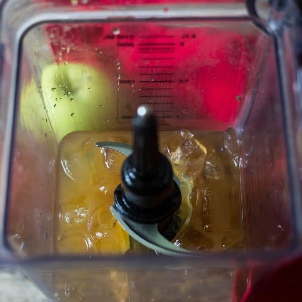 Looking down into an open blender filled with apple cider, caramel vodka and ice to make an apple cider vodka slush