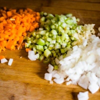 Chopped carrots, celery, onions,garlic, and ginger on a wooden cutting board. The base of a great pumpkin soup